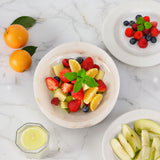 Fruit salad with strawberries, blueberries, and lemon slices in a bowl on a marble surface.