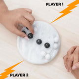Two hands reaching towards a round white game with black marbles on a beige background, labeled 'Player 1' and 'Player 2'.