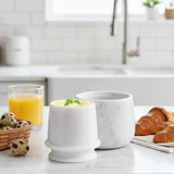 White marble butter crock with butter displayed on a kitchen counter alongside breakfast items.