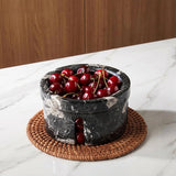 Black marble bowl filled with cherries on a woven coaster