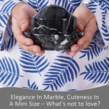 Hands holding a mini black marble butter crock with lid.