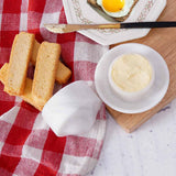 marble butter crock with lid holding butter, placed on a table with bread and a knife.