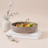 Decorative stone bowl with cherries on a beige surface with a vase and branches.