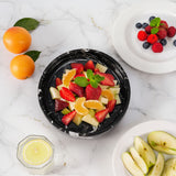 Fruit salad in a black bowl with oranges, strawberries, and other fruits on a marble surface.