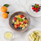 Fruit salad in a bowl with oranges, strawberries, blueberries, and apples on a marble surface.