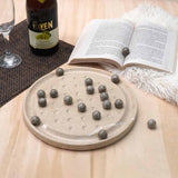Round stone coaster with spherical stones on a wooden surface next to an open book and bottle of wine.