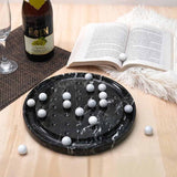 Black marble board with white spherical objects on a wooden surface with a book and bottle in the background.