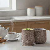 Two stone-textured butter dish with steam rising from a cup on a kitchen counter.