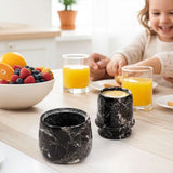 Black marble butter keeper on a family breakfast table with juice and fruit.
