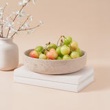 Bowl of cherries on stacked books with a vase of flowers on a beige background