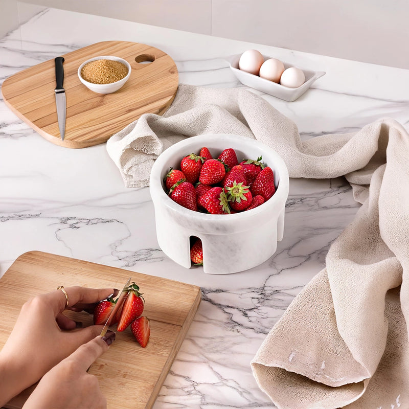 Person slicing strawberries on a wooden cutting board with a bowl of strawberries and eggs in the background.