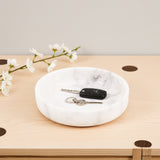 White marble-patterned tray with keys on a wooden surface with flowers in the background