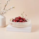 Bowl of cherries on a stack of books with a vase and flowers in the background