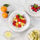 Fruit salad with strawberries, oranges, and apples on a marble surface.