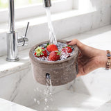 Person washing strawberries under running water from a faucet using a stone-like container.