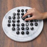 Round marble board with white and black marble balls on a wooden surface