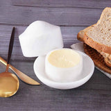 White marble butter crock with lid holding butter, placed on a table with bread and a knife