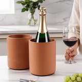 Bottle of champagne in a terracotta cooler with a glass of red wine on a marble surface.