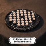 A polished black marble solitaire board with multiple round beige marble balls arranged on top, shown on a dark textured surface. A label at the bottom reads 'Polished Marble Solitaire Board'.