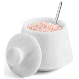 A white marble salt container with its lid off, filled with pink Himalayan salt and topped with a metal spoon, on a white background.