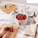 Person cutting strawberries on a wooden board with a bowl of strawberries and eggs in the background.
