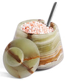 A decorative salt Cellar , shown open with pink salt inside and a metal spoon. The matching round lid rests in the foreground on a clean white background.
