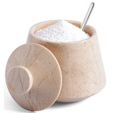 A beige stone-style salt and pepper shaker container with its lid off, filled with white salt and a silver metal spoon, on a white background.
