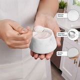 A person in a white kitchen setting holds a small white marble salt or sugar bowl with a stainless steel spoon, with three circular callout insets showing the natural marble finish, stainless steel spoon, and sturdy base.