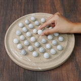 Hand interacting with white balls objects on a round beige board on a wooden surface