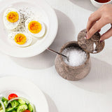 A marble-style salt and pepper shaker container with a lid being lifted by a hand.