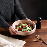 Marble salad bowl filled with fresh vegetables and greens, held by hands on a wooden table.