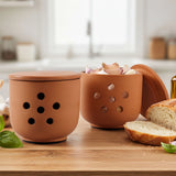  Two terracotta containers with different designs on a wooden surface with bread and herbs.