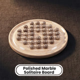 A polished marble solitaire board with multiple small polished marble balls arranged on it, shown on a dark textured fabric background with a text label reading 'Polished Marble Solitaire Board'.