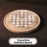 A travertine solitaire board made of natural beige stone, holding 25 smooth white travertine gemstone balls arranged in a grid. The board is set against a dark brown textured fabric background, with a white label at the bottom reading 'Travertine Solitaire Board'.