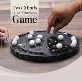 Two hands playing a game with white balls on a black board, text 'Two Minds One Timeless Game' above.