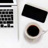 Laptop, smartphone, and coffee cup on a white surface
