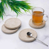 Set of stone coasters with a glass of tea and spoon on a marble surface.