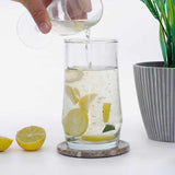 Pouring liquid into a glass with lemons and mint leaves on a white surface.