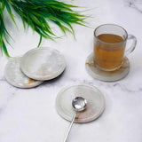 Set of marble coasters with a cup of tea and a spoon on a marble surface.