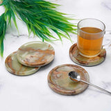 Set of marble coasters with a glass of tea on a marble surface with green leaves.