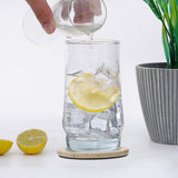 Person pouring liquid into a glass with lemon slices on a white surface