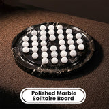 A polished black marble solitaire board with white marble veining, holding multiple white circular discs, shown on a brown textured surface with a label reading 'Polished Marble Solitaire Board'.