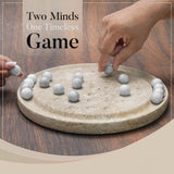 Two hands playing with marble-like objects on a stone board, with text 'Two Minds One Timeless Game' above.