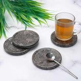 Set of stone coasters with a glass of tea and spoon on a marble surface.