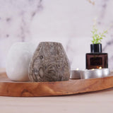 Decorative items including a white candle, textured stone, and a small plant on a wooden tray with a blurred background.