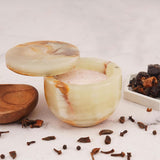 Decorative stone container with a wooden lid on a white surface with spices around