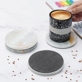Black and white striped mug on a marble coaster with a hand holding it, surrounded by scattered coffee beans and a notebook.