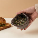 Hand holding a stone bowl filled with rosemary, with a beige background