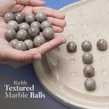 Hand holding marble balls with a plate of marble balls on a blue background