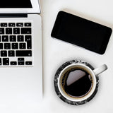 Laptop, smartphone, and coffee cup on a white surface